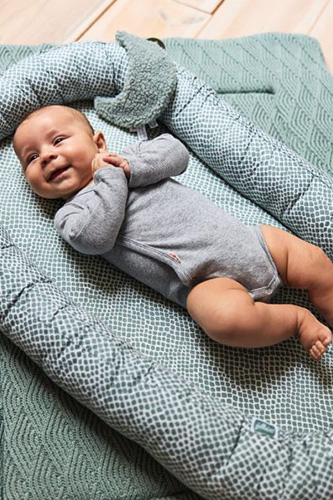Vol Verwachting - Blije baby die op een dekentje in een babynestje ligt