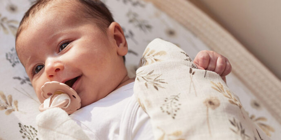 Vol Verwachting - Lachende baby met speen gewikkeld in hydrofiele doek